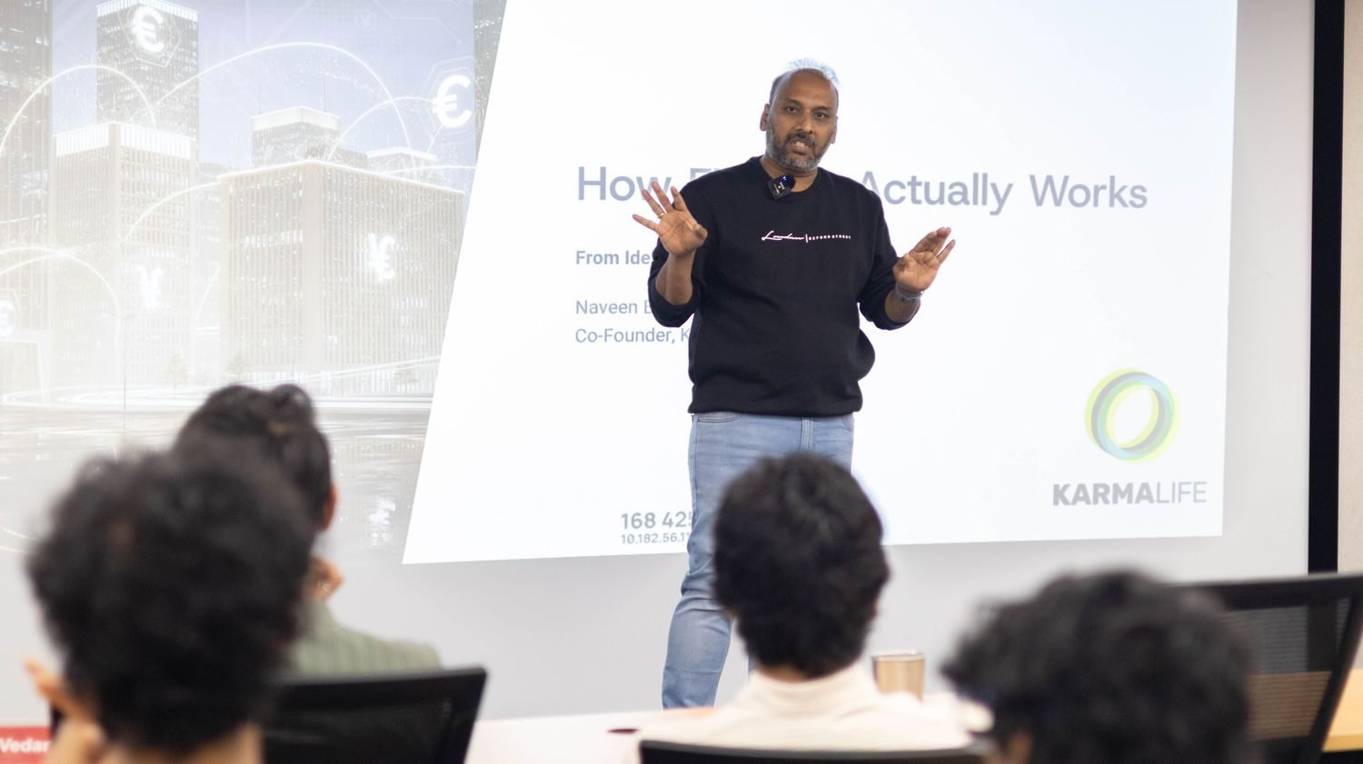Naveen Budda gesturing while presenting a slide titled 'How Fintech Actually Works' to Mesa School of Business students, with the KarmaLife logo visible on screen.
